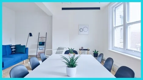 Moderner Besprechungsraum mit weißem Tisch, schwarzen Stühlen, Zimmerpflanzen und großen Fenstern in heller, minimalistischer Umgebung<br /><br />
