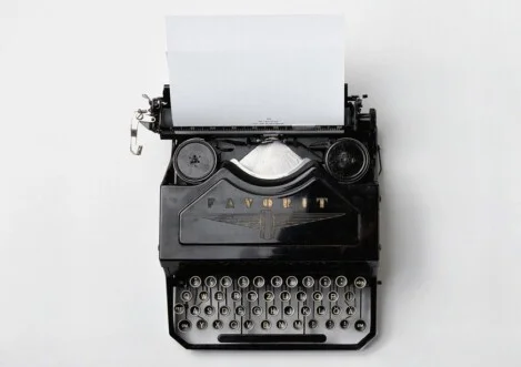 Schwarze, klassische Schreibmaschine mit eingespanntem Papier auf hellem Untergrund – von oben fotografiert